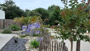 Un jardin où l’on trouve une variété de plantes, une clôture en bois et un chemin pavé.