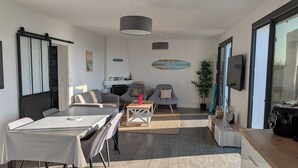 Een moderne woonkamer met een eethoek, een zithoek, een salontafel en een aan de muur bevestigde televisie.