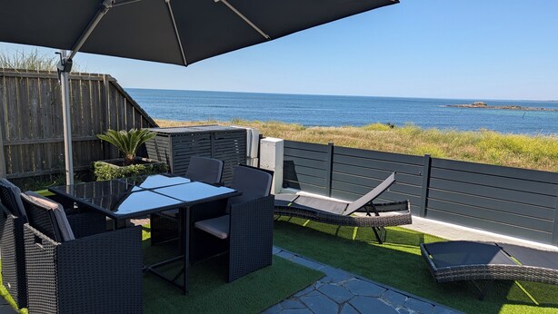 Een terras buiten met een tafel, stoelen, een houten omheining en uitzicht op zee.