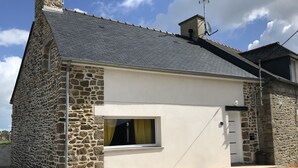 Un edificio de piedra con un ventanal pequeño, una puerta, una antena parabólica y una chimenea.