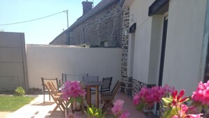 Un patio con mobiliario exterior y plantas florecientes de color rosa.