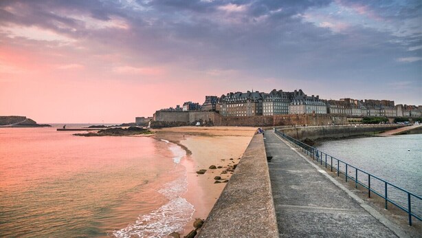 Un paisaje urbano costero con una imponente fortificación histórica y un paseo marítimo a lo largo de la costa.