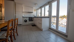 A modern kitchen with white cabinets, a washing machine, and a dining area with wooden chairs. - At the gates of Strasbourg charming apartment in lush greenery 4 per. (Eckbolsheim)