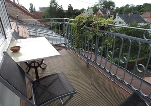 Ein Balkon mit Tisch, zwei Stühlen, einer Kübelpflanze und einem Metallgeländer.