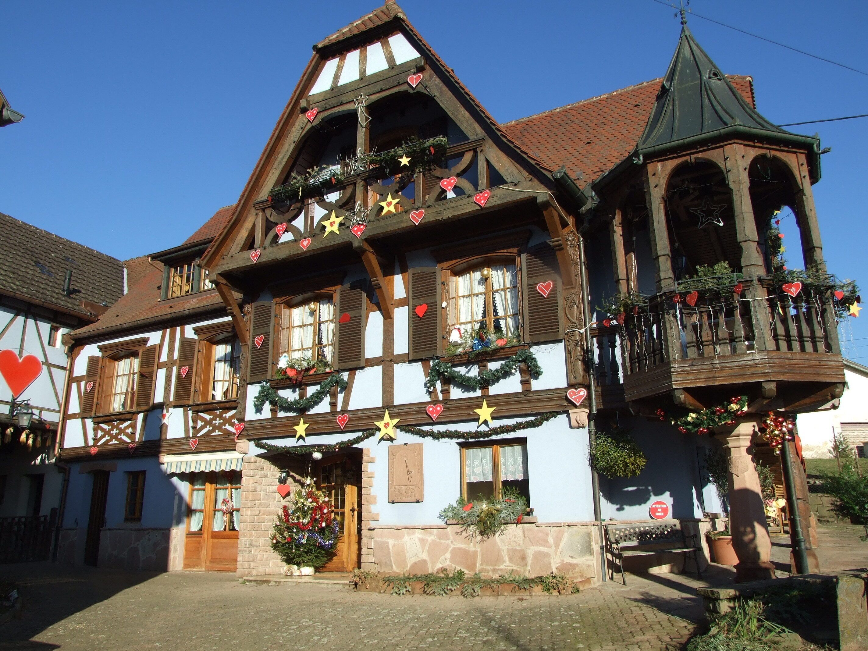 A traditional half-timbered building with a balcony and a bell tower, decorated with festive garlands and ornaments.