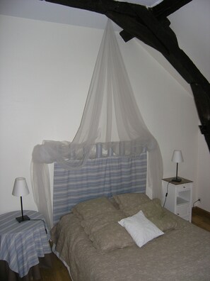 Quarto com cama de dossel, mesa de cabeceira com abajur e criado-mudo iluminado.