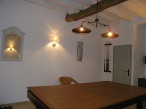 Uma sala de jantar com uma mesa de madeira, duas luminárias fixadas na parede, uma cadeira e uma porta.