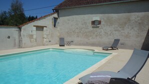 En swimmingpool med to liggestole og et lille vindue i en bygning.