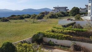 Un quartier résidentiel situé sur la côte, avec des maisons modernes, un terrain herbeux et une vue sur la mer et les montagnes lointaines.