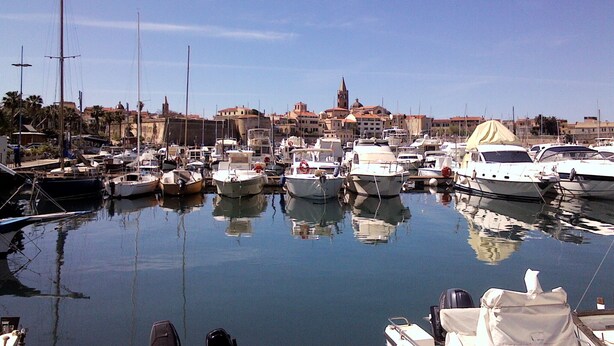 Un port de plaisance où sont amarrés différents types de bateaux, entouré de bâtiments et sous un ciel dégagé.