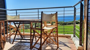 Un balcon avec une table et des chaises, donnant sur un paysage verdoyant et la mer.