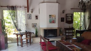 A cozy living room with a fireplace, wooden furniture, and a view of greenery outside. - Charming house, in a green setting, on the Landaise Coast (Labenne)