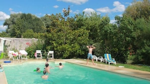 A swimming pool with people in the water, surrounded by trees and a stone wall.