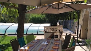 An outdoor patio with a table set for dining, surrounded by chairs, and shaded by a large umbrella.
