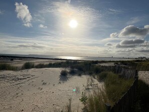 Una playa con dunas de arena, una cerca de madera y vistas al mar y al horizonte de la ciudad.