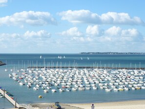 Uma marina com vários barcos atracados, uma praia de areia e um céu claro com nuvens.