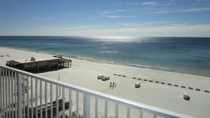 Blick auf einen Strand vom Balkon aus, mit einem Rettungsschwimmturm, Liegestühlen und blauem Himmel.
