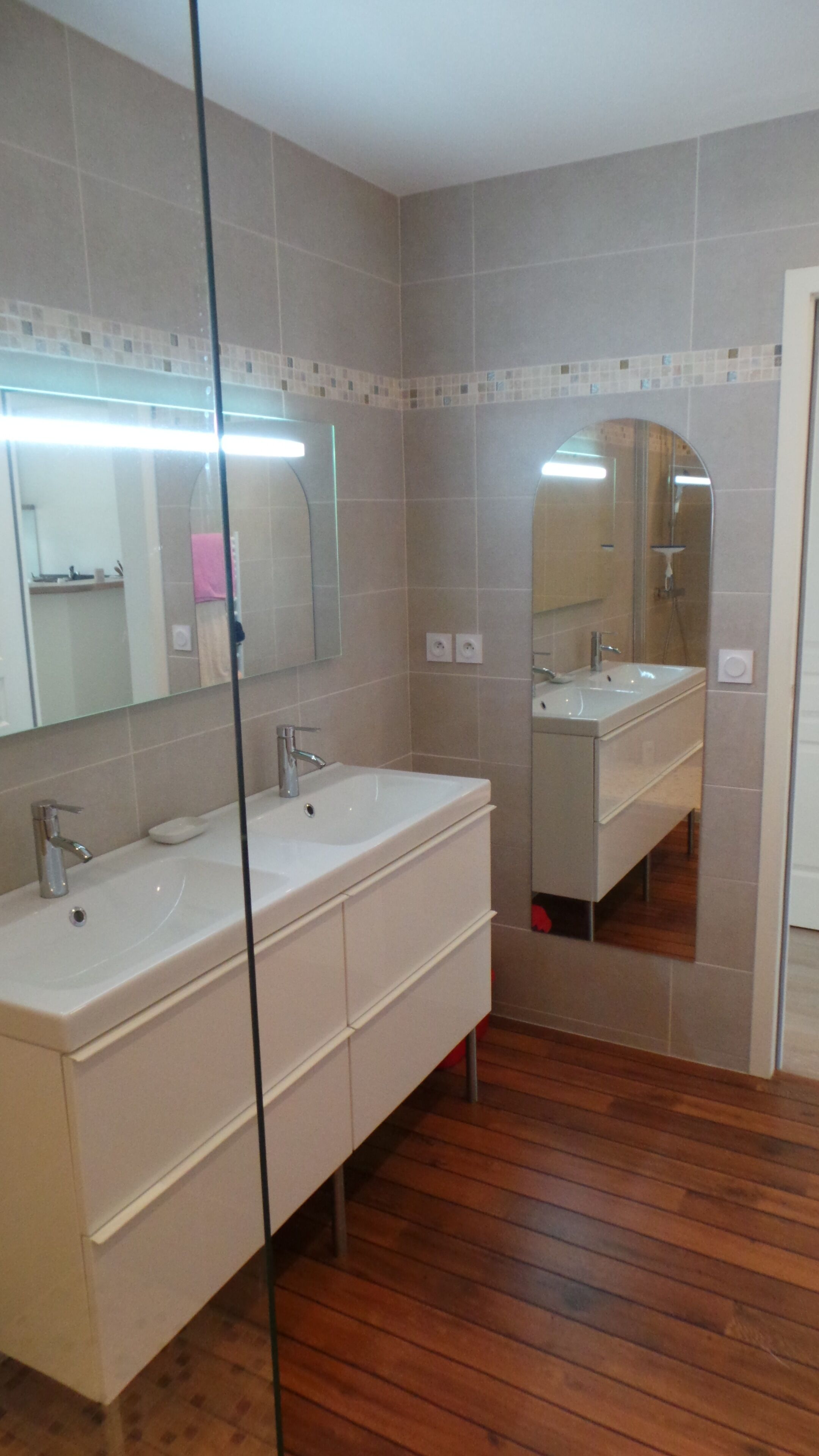 A bathroom with two sinks, a mirror, and wooden flooring.