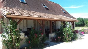 Un bâtiment de style rustique, évoquant une grange, avec un toit en tuiles, des poutres en bois et un porche abrité.