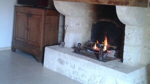 Une cheminée avec un foyer en pierre, une étagère en bois au-dessus et un téléviseur posé sur un meuble en bois, à gauche.
