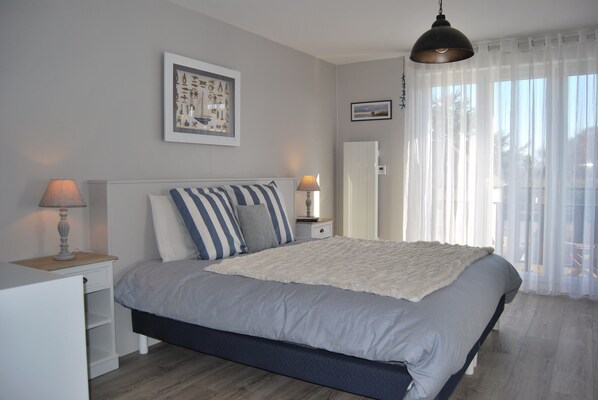 A bedroom with a bed, bedside tables, a lamp, a framed picture, and a window with curtains.