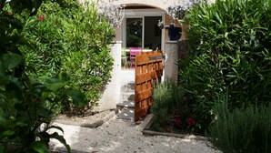 Un vialetto nel giardino conduce a un edificio con una porta scorrevole in vetro, immerso nel verde e delimitato da una recinzione in legno.