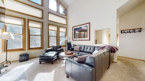 A spacious living room with large windows, a leather sofa, a coffee table, and a lamp. - Snowcreek #880 3 Bedroom Condo by RedAwning (Mammoth Lakes)