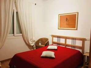 A bedroom with a red bedspread, two pillows, a wicker chair, a wooden headboard, and a framed picture on the wall. - NON-SEMI-DETACHED HOUSE WITH PRIVATE POOL WIFI AIR CONDITIONING NEAR BEACH RIELLS (L'Escala)