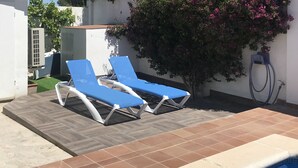 Un área junto a la piscina con dos sillas reclinables azules y una pequeña estructura blanca.