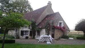 Een rustiek stenen huis met schuine kap, een klein terras en een grindpad.