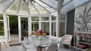 Ein Wintergarten mit einem Glastisch, weißen Stühlen und einem Korbstuhl.