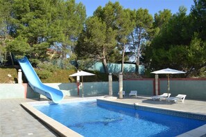 Une piscine avec un toboggan bleu, des chaises longues et des parasols.