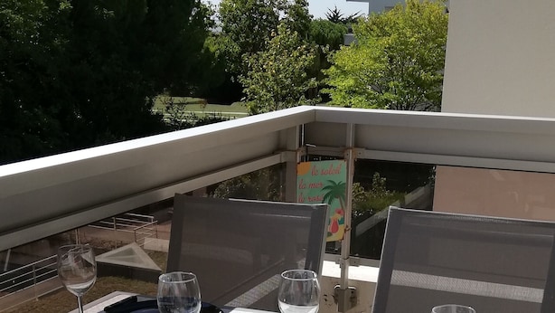 Mesa de comedor dispuesta con platos, cubiertos y copas de vino, rodeada de sillas en una terraza al aire libre.
