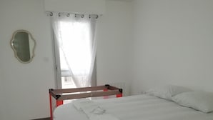 Un dormitorio con cama, mesita de noche, espejo y ventana con cortinas.