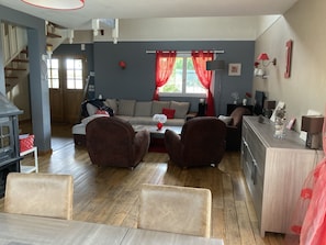 Ein gemütliches Wohnzimmer mit einer Couch, zwei Sesseln, einem Couchtisch und einem Kamin. Eine Treppe führt zu einer oberen Ebene.