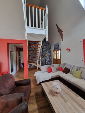 A spacious living area with a high ceiling, a staircase, a sofa set, and a wooden coffee table.
