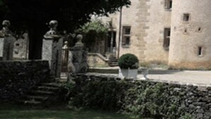 Ein Steinhaus mit einem Turm, umgeben von einem gepflegten Garten und Statuen.