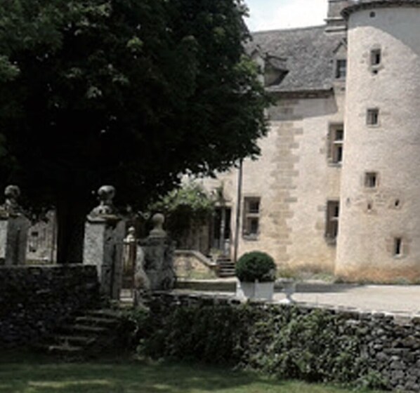 A stone building with a tower, surrounded by a well-maintained garden and statues.