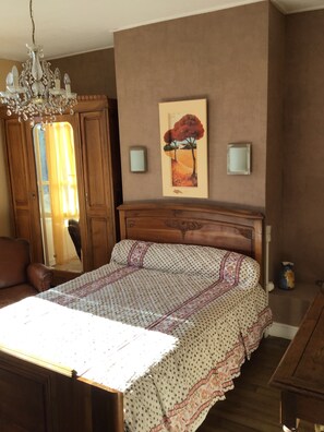 A bedroom with a wooden bed, a chandelier, a painting on the wall, and a mirror.