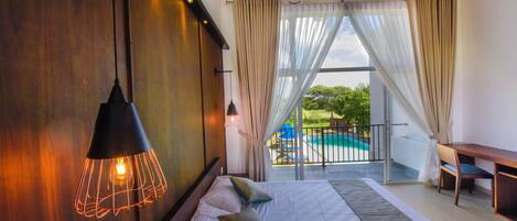 A bedroom with a large bed, a hanging light fixture, and a view of a swimming pool.