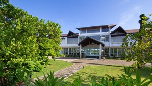 A modern building with a covered entrance, surrounded by lush greenery and a paved pathway. - Subaseth Villa (Nuwaragam Palatha Central)