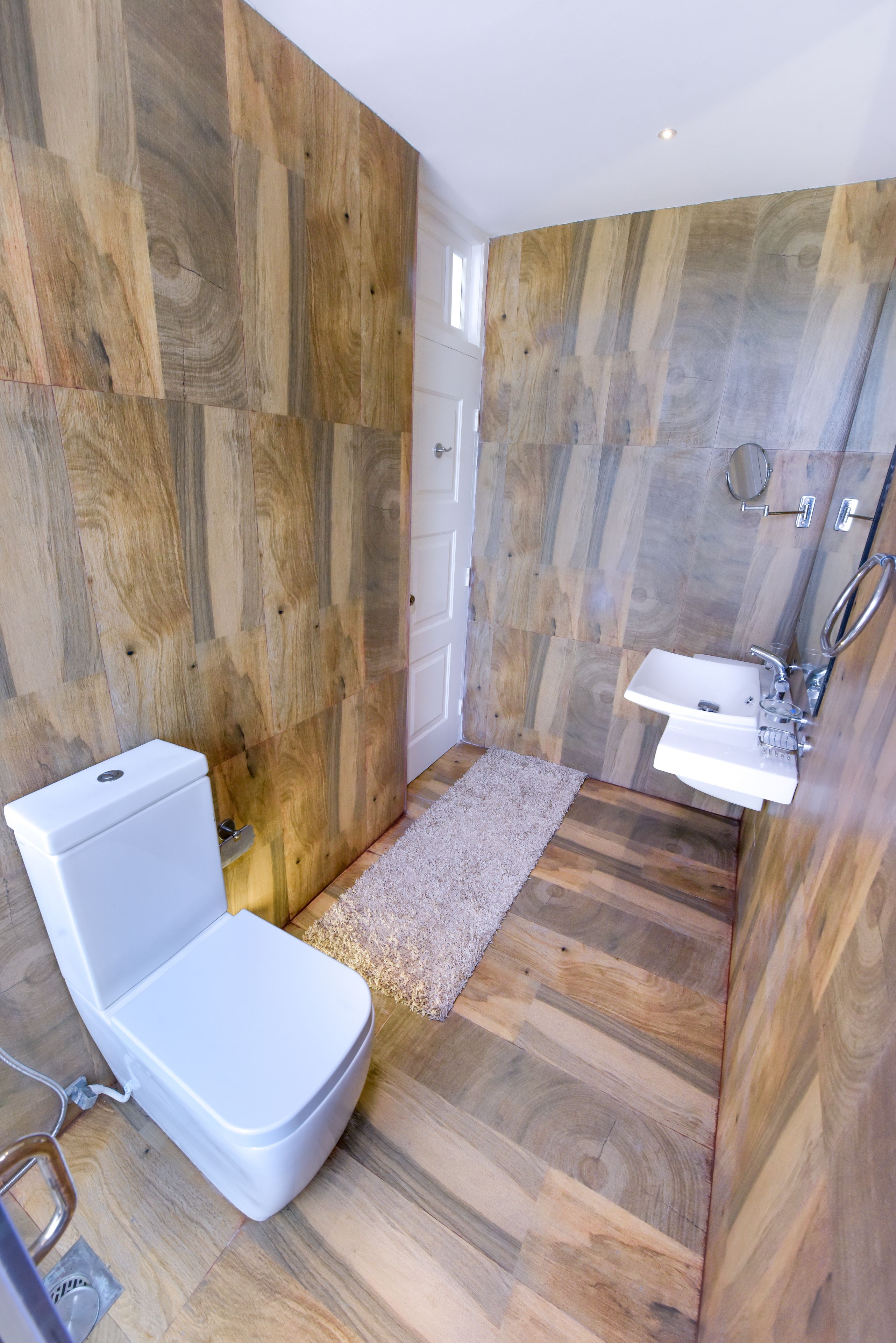 Un baño con suelo de madera, inodoro, lavabo y zona de ducha.