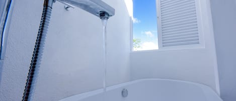 Una bañera blanca con un caño visible y una ventana con persianas.