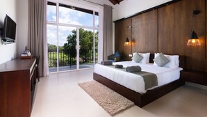 A bedroom with a large bed, a TV on the wall, a wooden headboard, and a view of the outdoors through a sliding door. - Subaseth Villa (Nuwaragam Palatha Central)