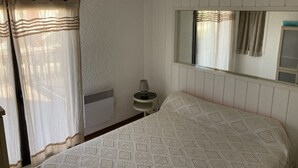 Un dormitorio con cama, mesita de noche con lámpara, ventana con cortinas y radiador.