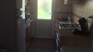 Cocina compacta con refrigerador, microondas, estufa y lavamanos. Una ventana proporciona luz natural y el espacio tiene piso de cerámica.