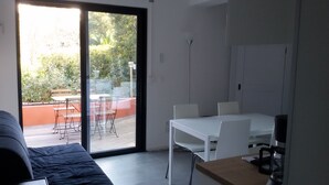 A modern room with a sliding glass door leading to an outdoor patio area. Inside, there is a white dining table with chairs, a sofa, and a small table with a coffee maker. - Nice air-conditioned 3rooms 3***in ground floor, private terrace , swimming pool (Saint-Raphaël)