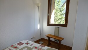 Een slaapkamer met een bed, nachtkastje, vloerlamp en een raam met uitzicht op bomen.