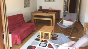 Een gezellige woonkamer met een rode bank, een houten bijzettafeltje en een grijze fauteuil.