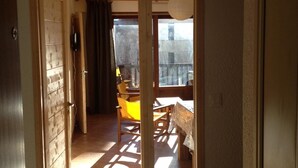 Een kamer met een houten vloer, een eettafel met stoelen, een hanglamp en een uitzicht door een deur naar een buitenbalkon.